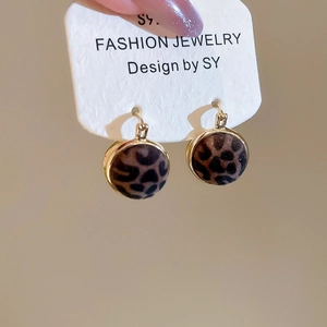 Detail of round leopard print earrings with a gold metal frame on a white jewelry card