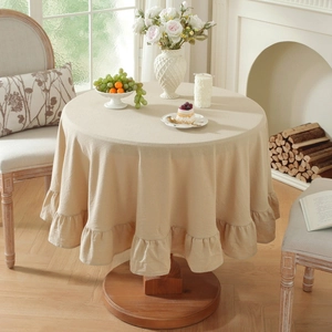 Detail of a beige linen round tablecloth with ruffled edge on a wooden table