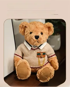 Close-up of brown teddy bear plush wearing a knit sweater with Teddy foot embroidery