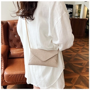 Beige Umschlag-Clutch mit goldener Kette, präsentiert von einem Model im modernen Café