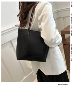 Close-up of a large black leather tote bag worn over the shoulder with a white blazer