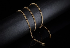 Detailed close-up of a gold Cuban link titanium steel chain necklace on a black display