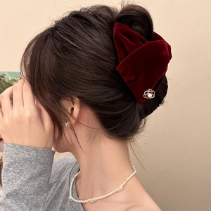 Close-up of a burgundy velvet bow hair clip with a golden camellia and pearl detail