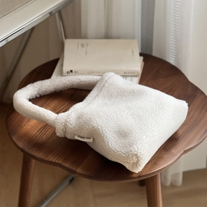 Detail of soft white faux fur handbag featuring simple wish label on dark wood stool