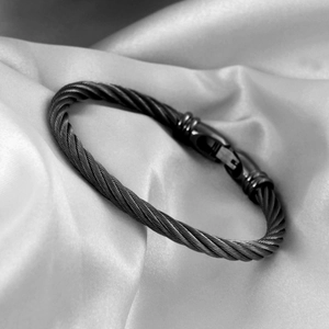 Macro detail of black twisted cable bracelet with a secure mechanical clasp on silk