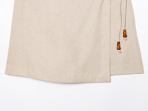 Détail d'une jupe en lin beige avec cordon de serrage latéral et perles en bois marron