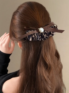 Close-up of leopard print bow hair clip with large cream pearl on brown wavy hair