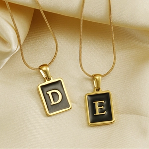Détail de colliers chaîne serpent dorés 18 carats avec pendentifs lettres D et E noirs