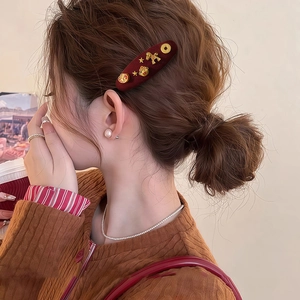 Red velvet hair clip with gold lucky cat charms on a woman's low bun hairstyle