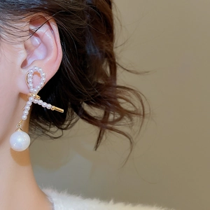 Primo piano di orecchini a fiocco dorati con grandi perle bianche su modella elegante
