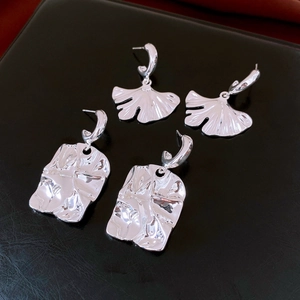 Detail view of silver ginkgo leaf and irregular square stud earrings on black surface