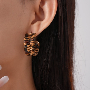 Close-up of leopard pattern C-shape woven leather earrings worn on model's ear