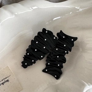 Macro detail of two black polka dot hair clips with ruffled texture on a ceramic plate