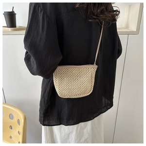 Dettaglio di una borsa a tracolla in paglia intrecciata beige con sottile tracolla su modella
