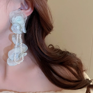 Détail de boucles d'oreilles fleurs en tulle bleu clair avec glands en cristal sur un mannequin