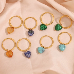 Close-up of heart-shaped natural stone pendants on gold hoop earrings over satin