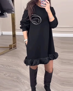 Détail de la fleur 3D blanche et de l'ourlet à volants sur une robe noire à manches longues