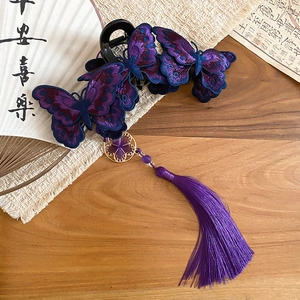 Dettaglio molletta per capelli a farfalla ricamata viola con nappa su tavolo in legno