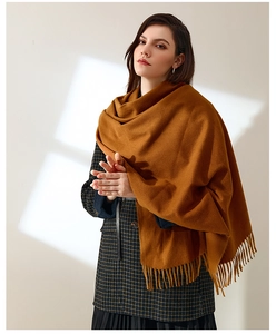 Detailed close-up of warm caramel scarf with elegant tassels on a female model