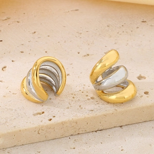 Detail of stacked two-tone gold and silver spiraled ear cuffs on a stone surface