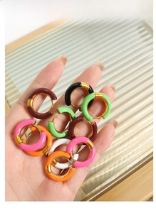 Close-up of vibrant enamel hoop earrings in multiple colors held against a glass background