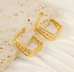 Macro detail of triple-layered gold square earrings with a textured twist on stone surface