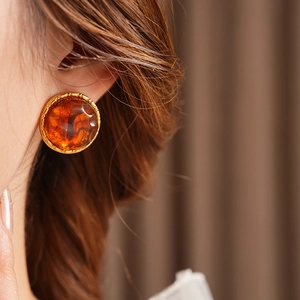Close-up of amber resin earrings in gold frame worn by a model in soft lighting