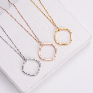 Minimalist square pendant necklace set in silver, gold, and rose gold on a white block
