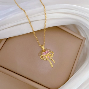 Elegant gold necklace with pink heart gemstone and bow pendant on beige jewelry box