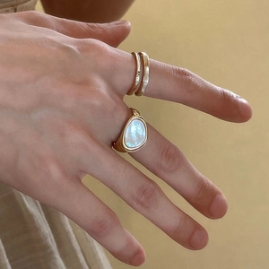 Detailed close-up of gold rings set with iridescent white gemstone and enamel on finger