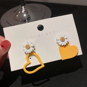 Detail of asymmetric daisy and yellow heart earrings on a white branded display card