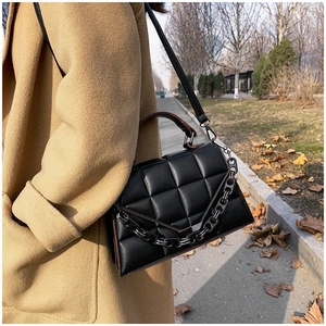 Detail of black quilted handbag with chain accent and brown strap on an outdoor street