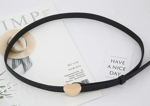 Flat lay of a thin black leather belt featuring a golden heart buckle on a magazine