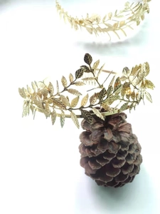 Detailed shot of golden laurel leaf headband with intricate metal leaf textures on pinecone