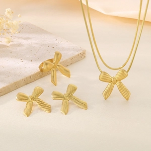 Elegant 18K gold-plated bow necklace and earring set on a minimalist stone background