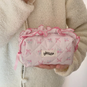 Pink quilted cosmetic bag with floral patterns and ruffled lace trim held by hand