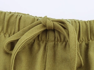 Detailed macro view of olive green linen trousers featuring elastic waist and drawstring