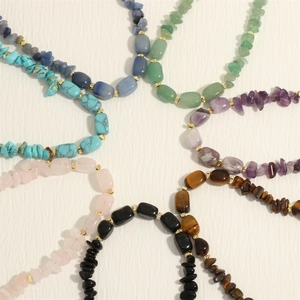 Macro shot of assorted natural gemstone chips and golden bead strands on linen base