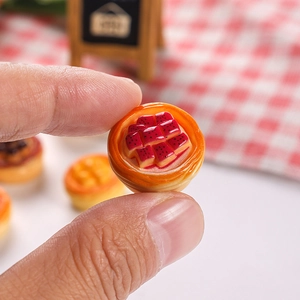 Miniature resin fruit tart dollhouse accessory shown between thumb and forefinger