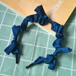 Close-up of dark blue twisted satin headband with elegant silk texture on green grid background
