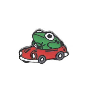 Détail d'un pin's en émail avec un petit crapaud vert conduisant une voiture rouge
