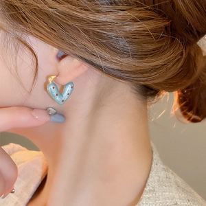 Close-up of heart-shaped earring with red polka dots on light blue base worn by model