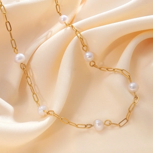 Detail of 18K gold stainless steel chain with freshwater pearls on cream satin fabric