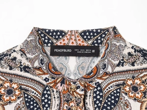 Détail du col à imprimé paisley avec étiquette en satin noir et bouton doré décoratif