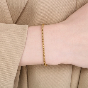Close-up of a gold stainless steel chain bracelet worn on a wrist over soft beige fabric