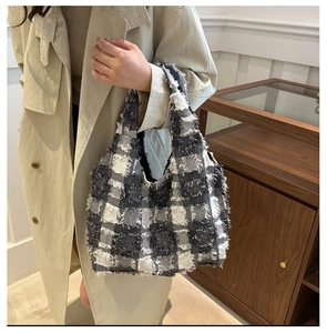 Detail of checkered tote bag with fringe edges held by a model in a beige coat