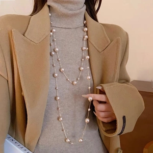 Détail d'un collier de perles multicouches sur manteau camel et pull gris élégant