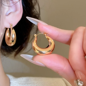 Gros plan de boucles d'oreilles créoles dorées polies portées sur l'oreille en métal
