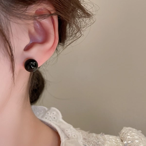 Close-up of elegant black spherical stud earrings worn with white lace top for women