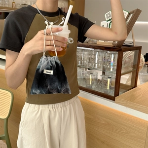 Close-up of tie-dye corduroy drawstring bag with woven label held in a cafe setting